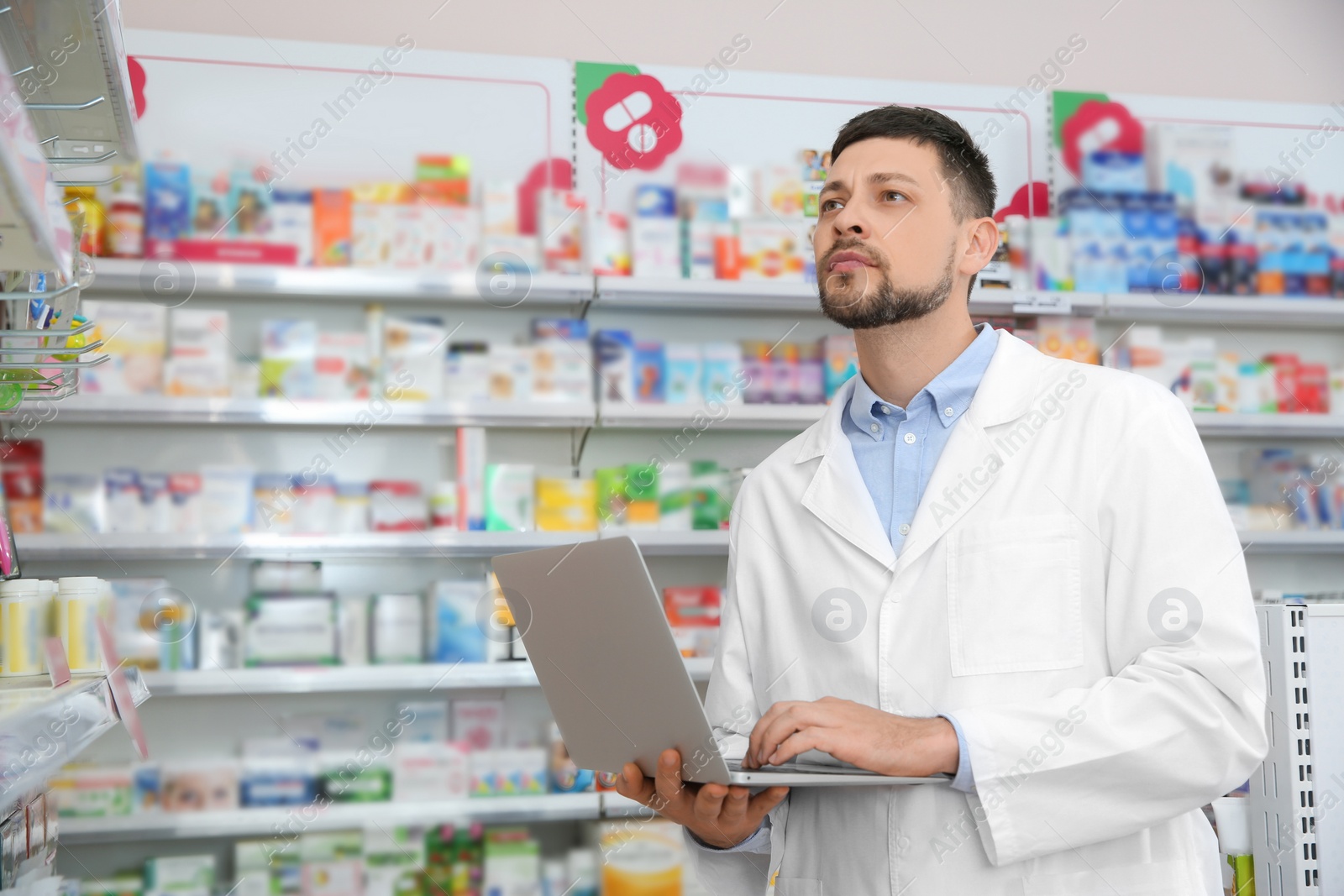 Photo of Concentrated pharmacist with laptop in modern drugstore