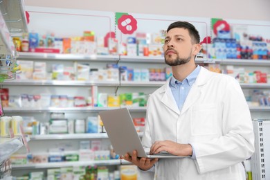 Photo of Concentrated pharmacist with laptop in modern drugstore