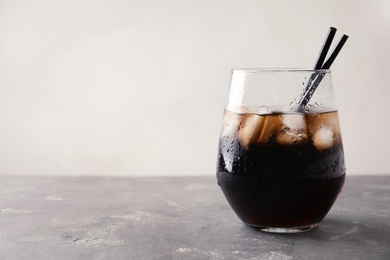 Photo of Glass of refreshing cola with ice on grey table. Space for text