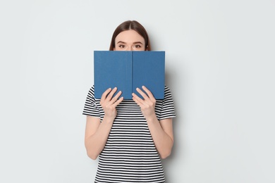 Photo of Young woman hiding behind book on white background, space for text. Reading activity