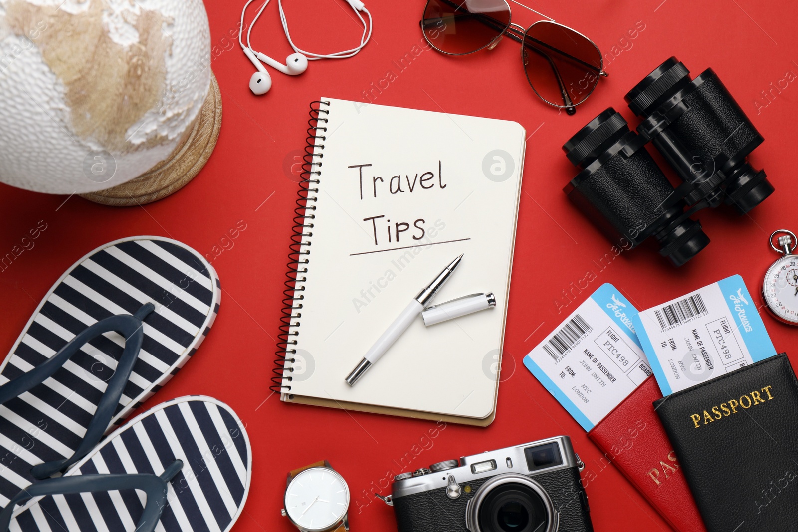 Photo of Flat lay composition with phrase Travel Tips written in notebook, passports, tickets and binoculars on red background