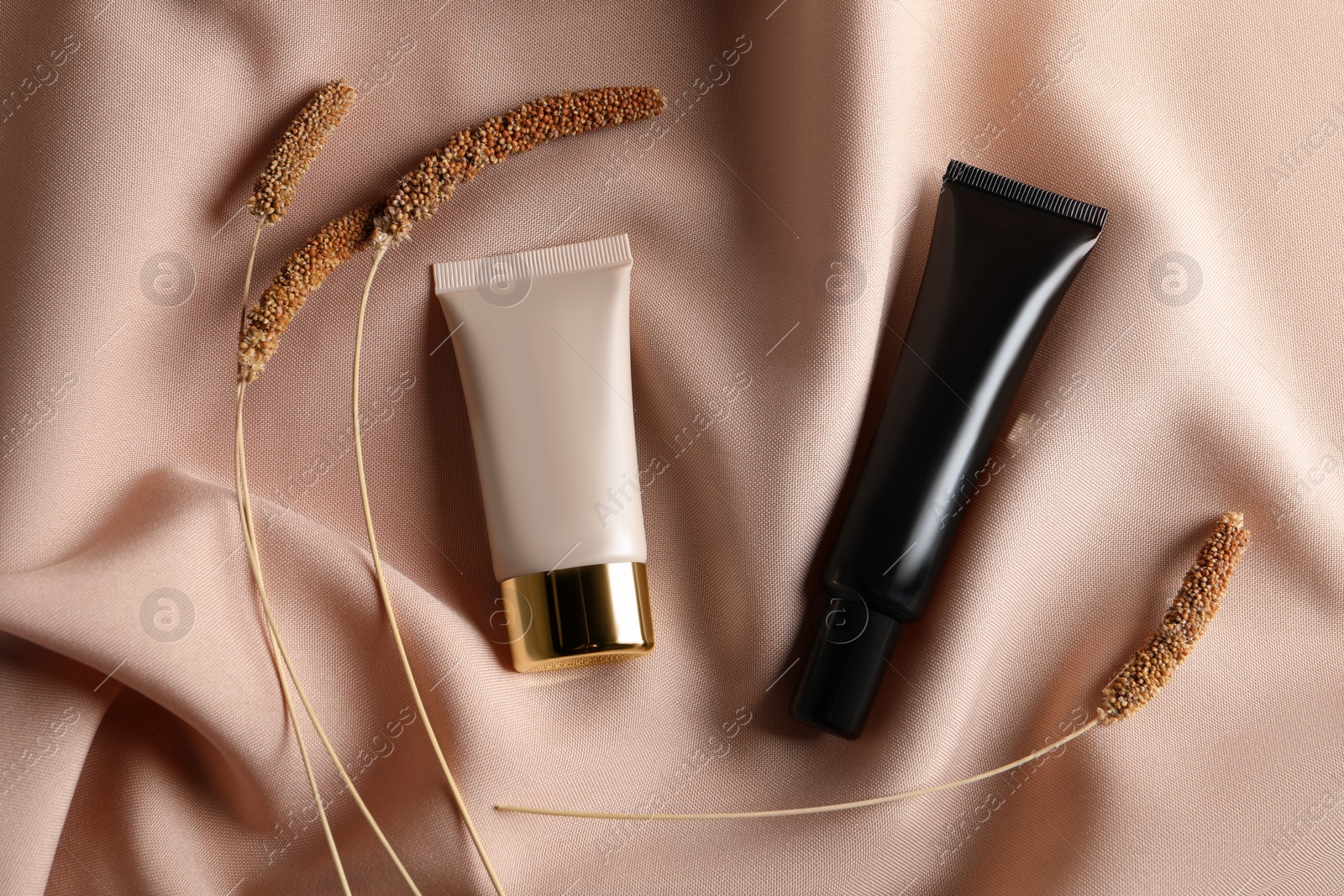 Photo of Tubes of skin foundation and decorative plants on beige cloth, flat lay. Makeup product