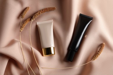 Tubes of skin foundation and decorative plants on beige cloth, flat lay. Makeup product