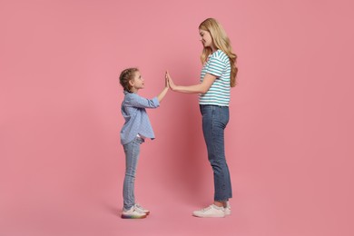 Mother and daughter giving high five on pink background