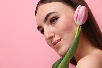 Photo of Beautiful woman with fake freckles and tulip on pink background, closeup. Space for text
