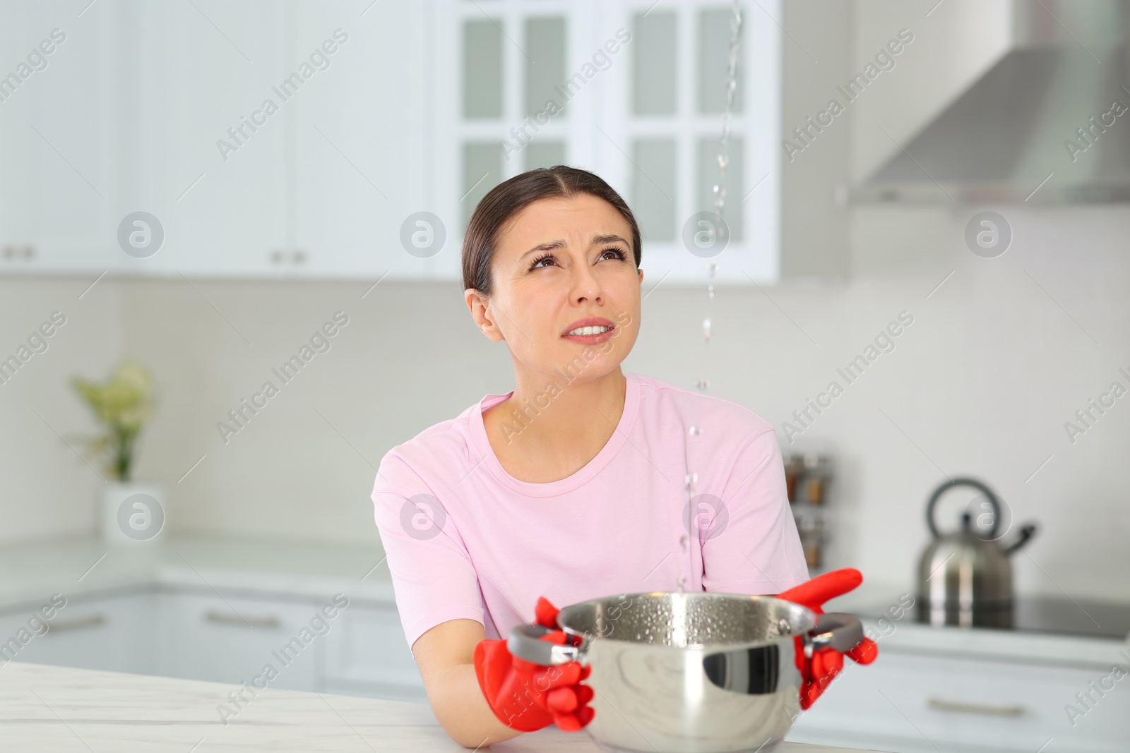 Photo of Young woman collecting leaking water from ceiling in kitchen. Time to call roof repair service