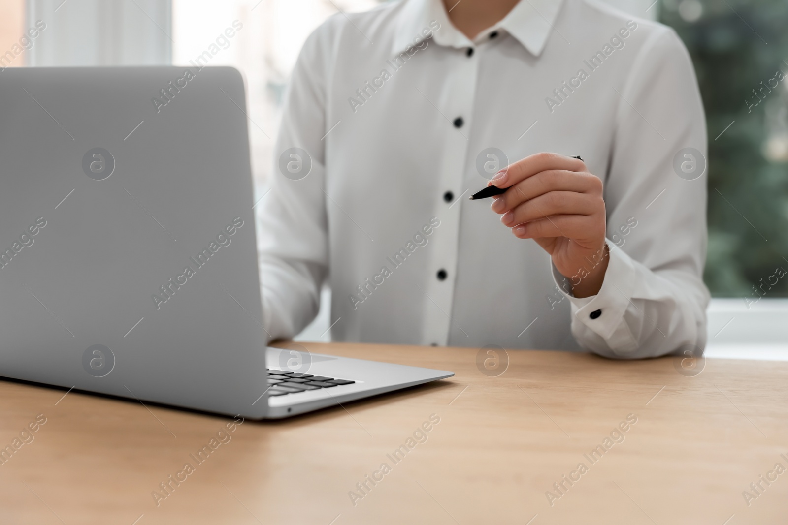 Photo of Woman with pen working on laptop at wooden table, closeup. Electronic document management