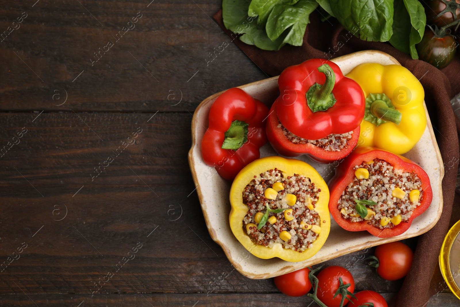 Photo of Quinoa stuffed bell peppers in baking dish, basil and tomatoes on wooden table, flat lay. Space for text