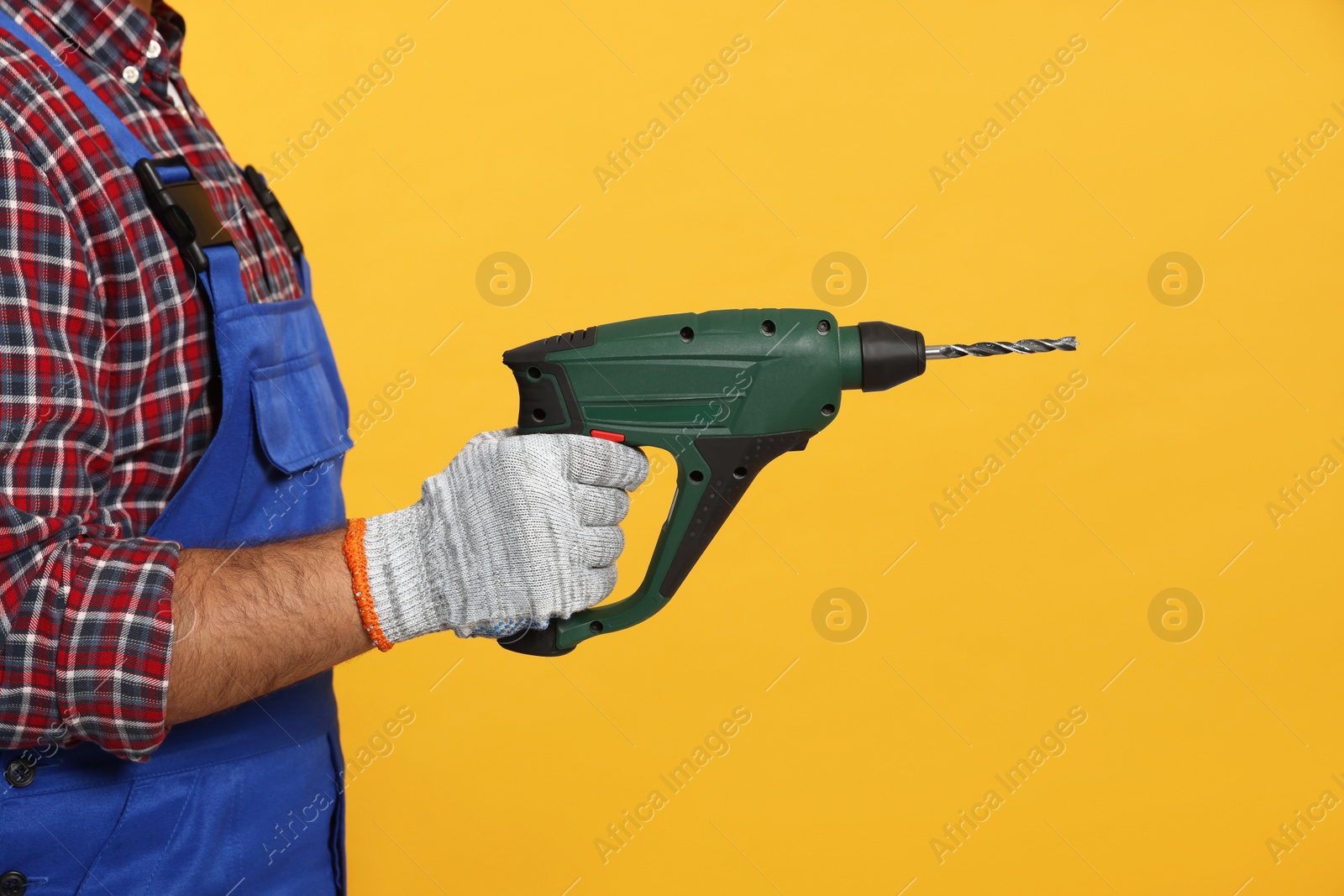 Photo of Worker in uniform with power drill on yellow background, closeup