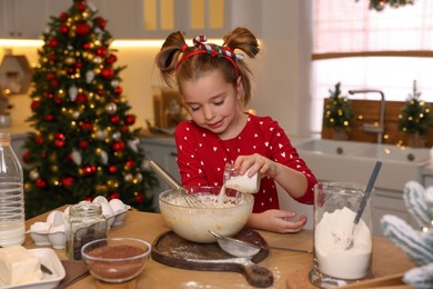 Cute little girl having fun while making dough for Christmas cookies in kitchen