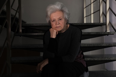 Portrait of poor mature woman sitting on stairs