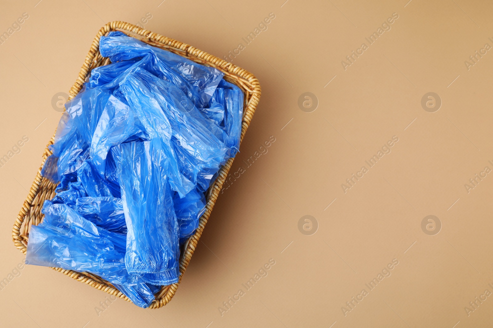 Photo of Blue medical shoe covers in wicker basket on beige background, top view. Space for text