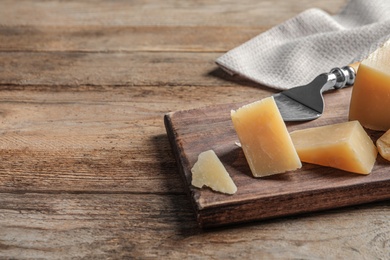 Board with cut Parmesan cheese on wooden table. Space for text