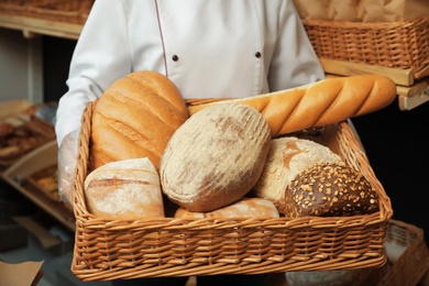 Photo of Professional baker with tray full of fresh breads in store, closeup