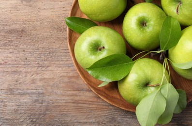 Photo of Fresh ripe green apples and leaves with plate on wooden table, top view. Space for text