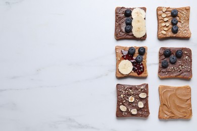 Photo of Different tasty toasts with nut butter and products on white marble table, flat lay. Space for text