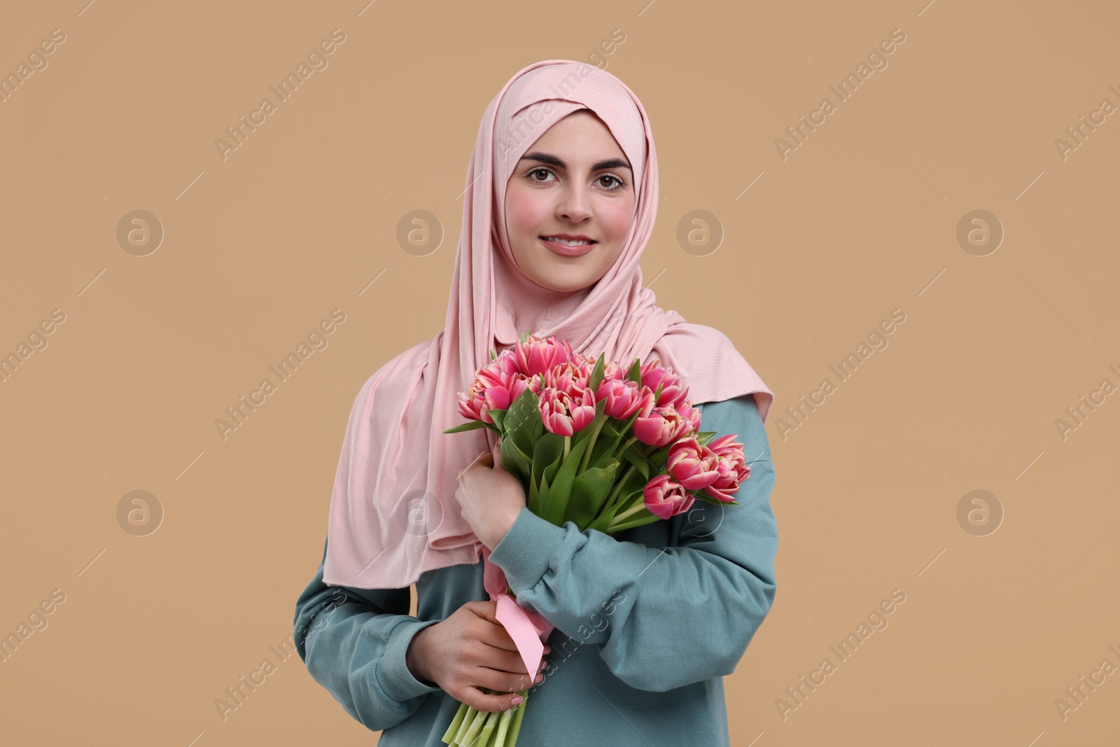 Photo of Happy woman in hijab with beautiful bouquet on beige background