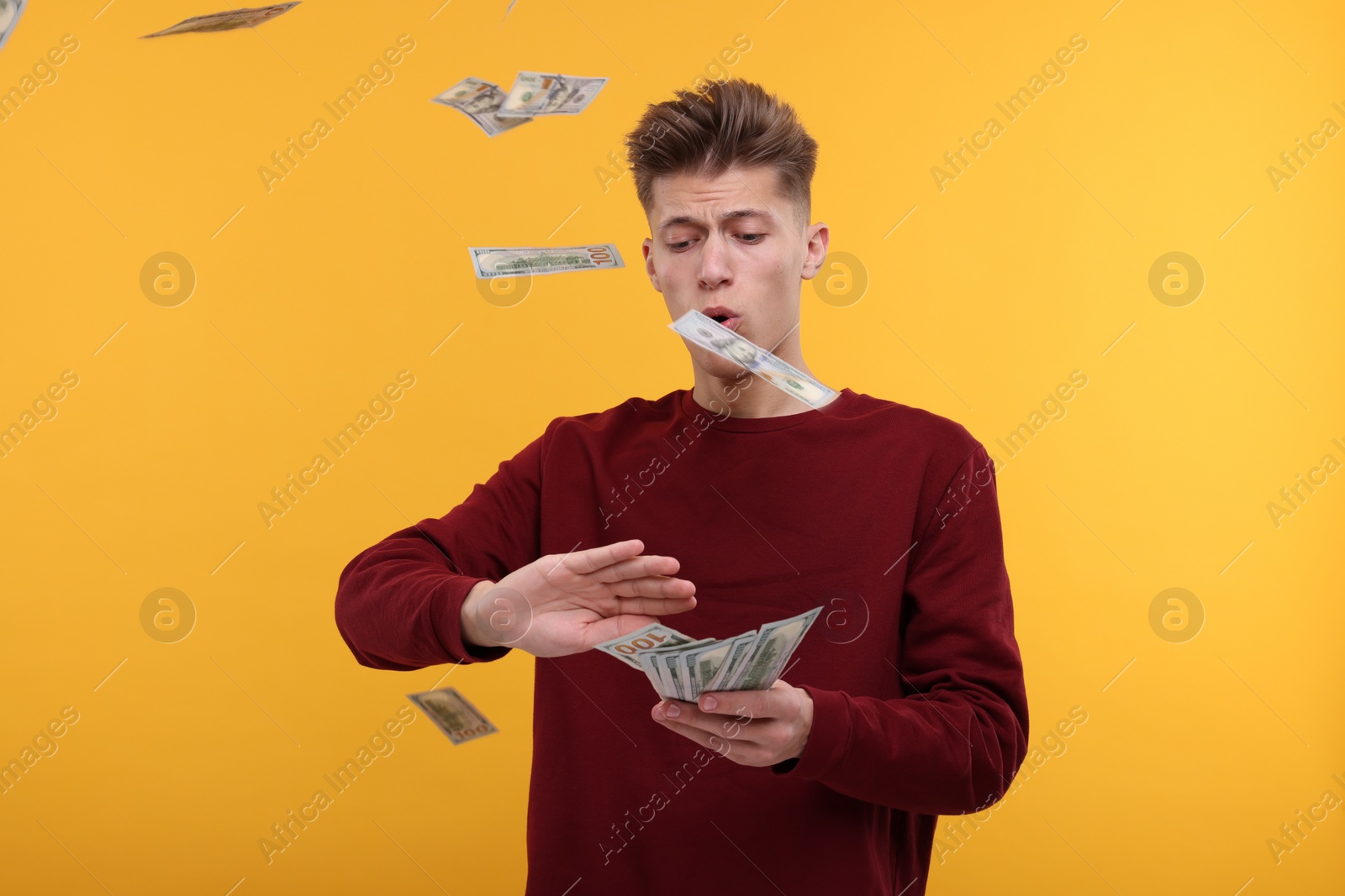 Photo of Handsome man throwing dollar banknotes on yellow background