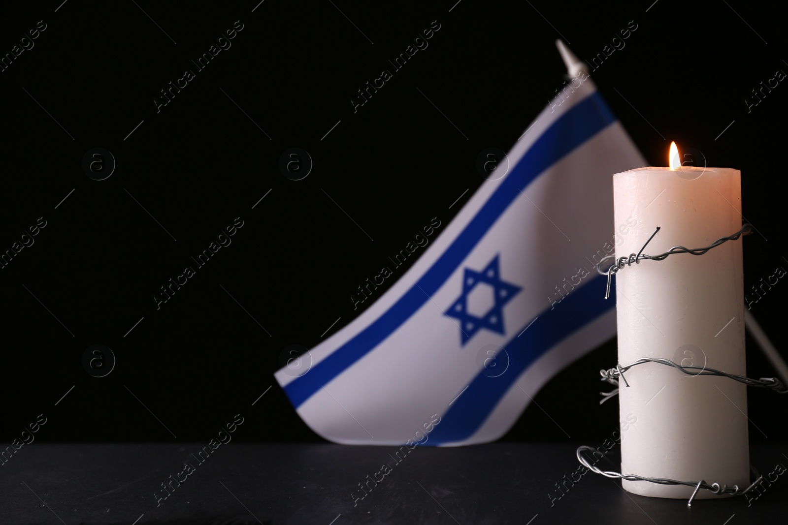 Photo of Barbed wire and burning candle on black background, space for text. Holocaust memory day