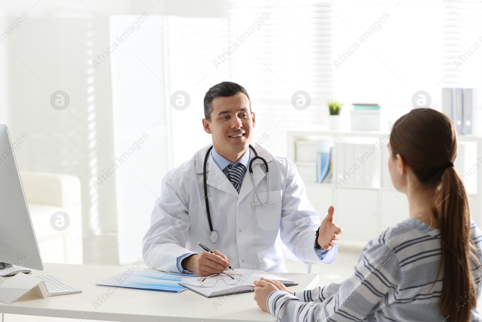 Photo of Doctor consulting patient at desk in clinic