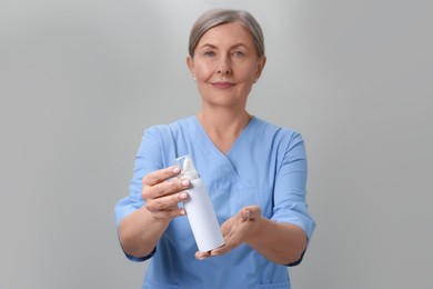 Photo of Woman holding nasal spray against light grey background, focus on bottle