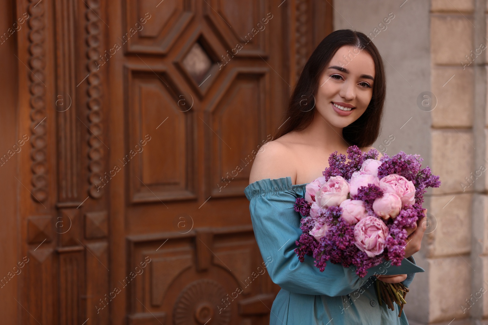 Photo of Beautiful woman with bouquet of spring flowers near building outdoors, space for text