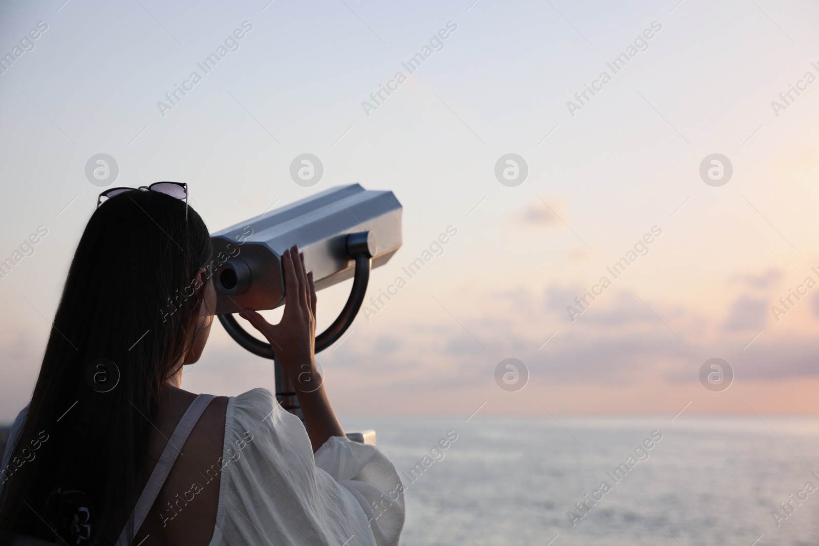 Photo of Young woman looking through tourist viewing machine at observation deck, back view. Space for text