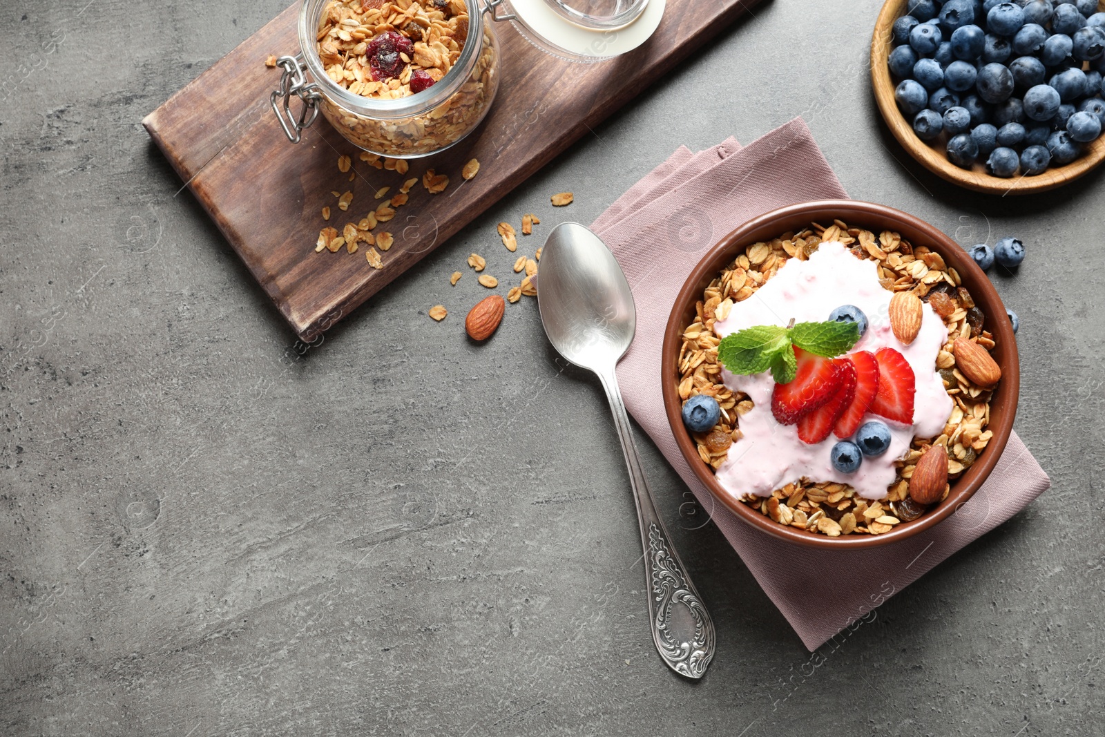 Photo of Delicious yogurt with granola and berries served on grey table, flat lay. Space for text