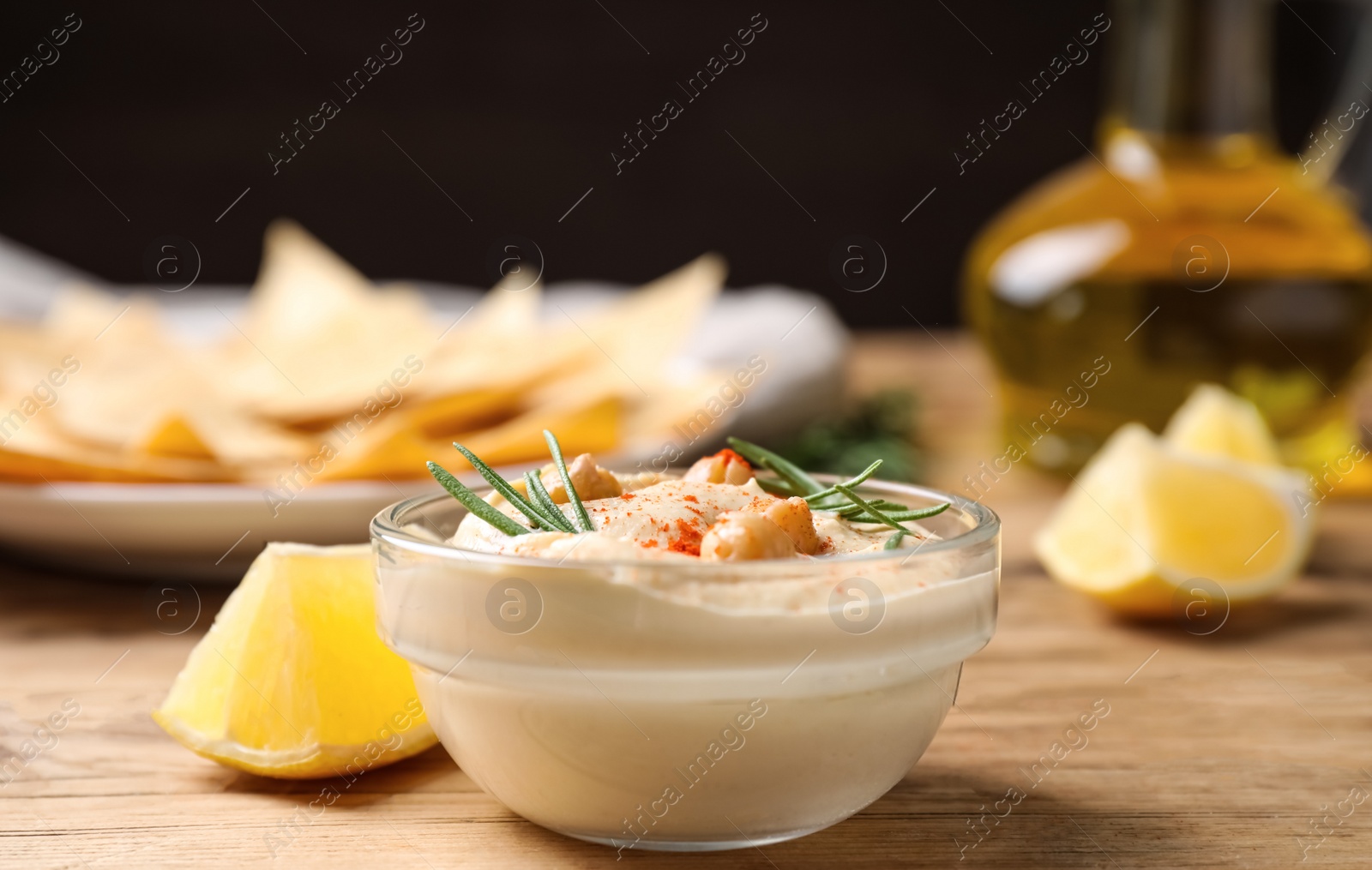 Photo of Delicious homemade hummus in glass bowl on wooden table