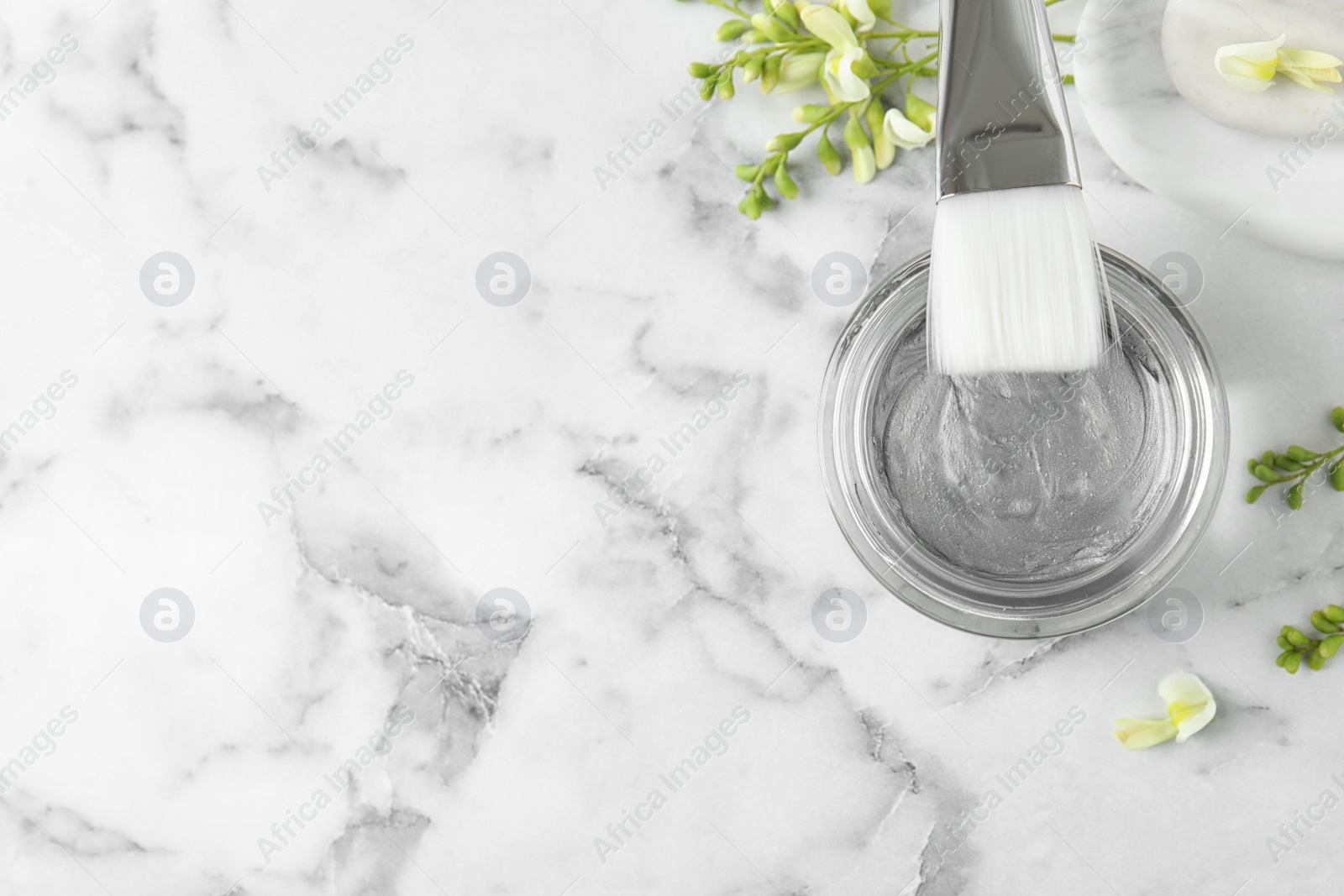 Photo of Professional face mask with brush and flowers on white marble table, flat lay. Space for text