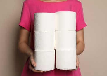 Photo of Woman with heap of toilet paper rolls on beige background, closeup