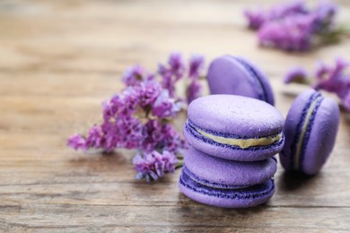 Photo of Delicious purple macarons and lilac flowers on wooden table, space for text