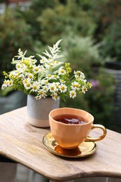 Photo of Cup of delicious chamomile tea and fresh flowers outdoors