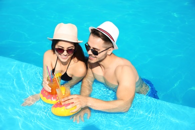 Young couple with refreshing cocktails in swimming pool on sunny day