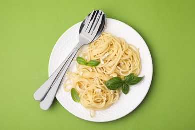 Delicious pasta with brie cheese and basil leaves on light green background, top view