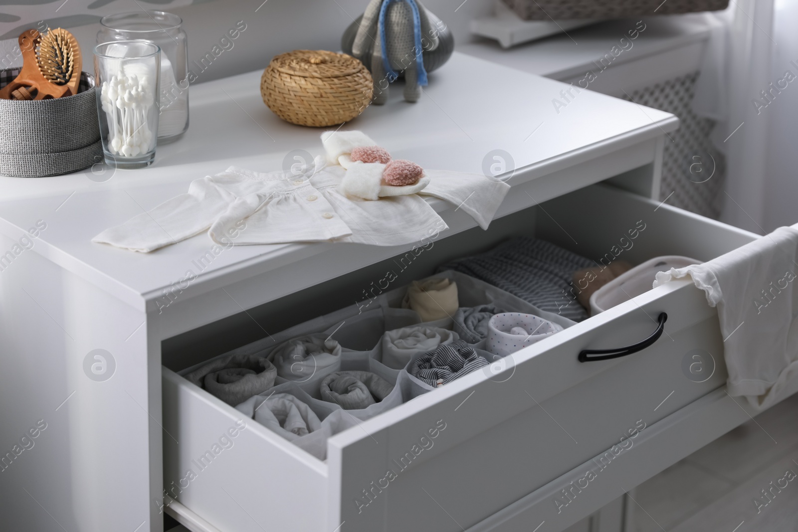 Photo of Modern open chest of drawers with baby clothes and accessories in room