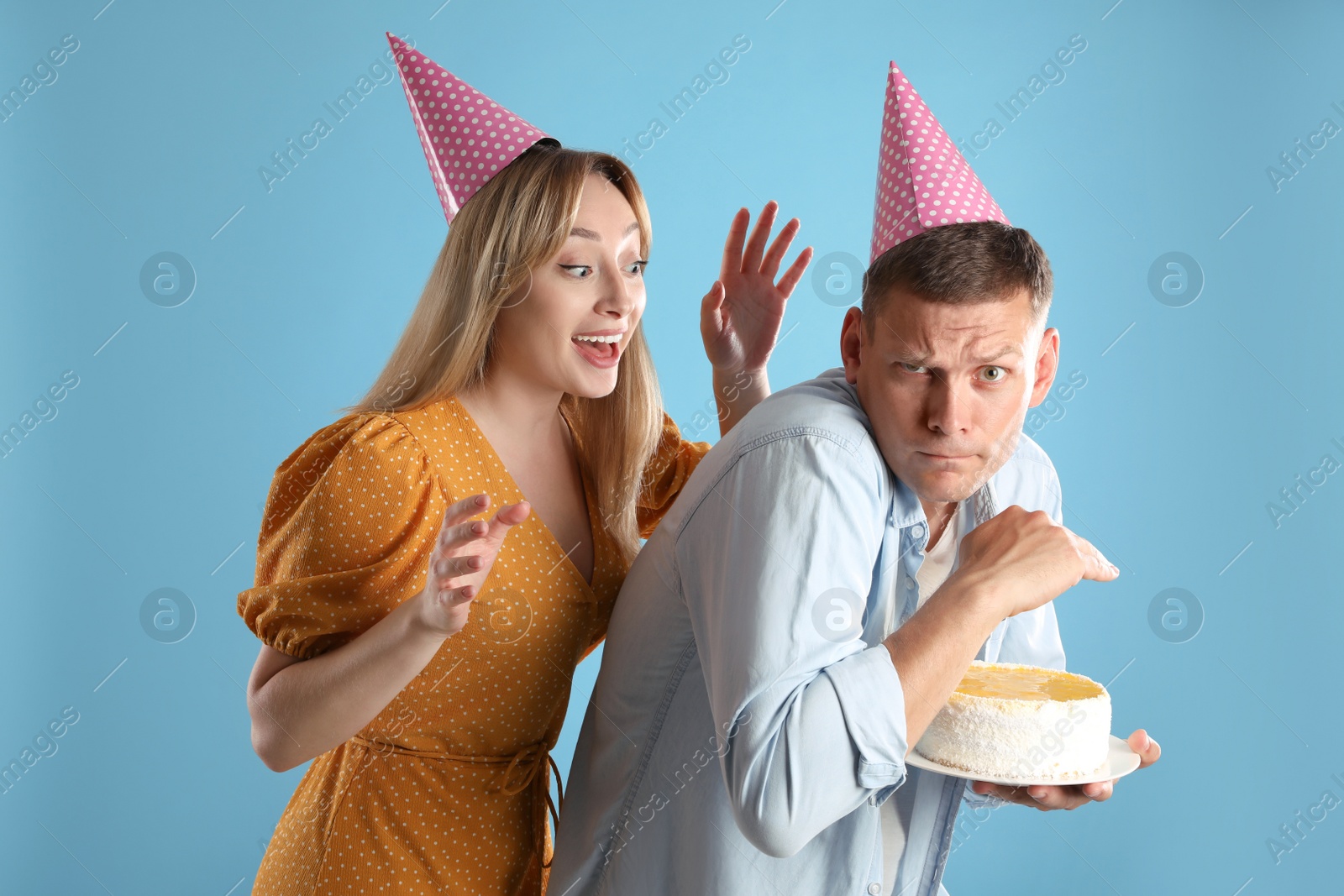 Photo of Greedy man hiding birthday cake from woman on turquoise background