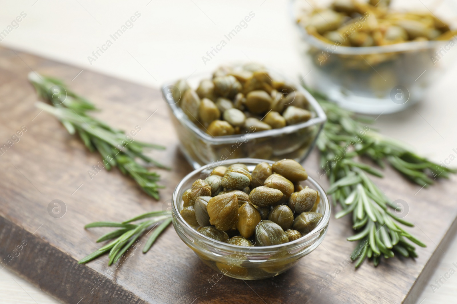 Photo of Delicious pickled capers and rosemary twigs on wooden board