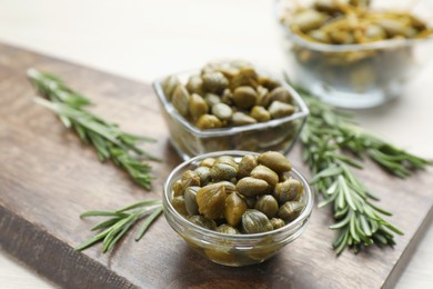 Photo of Delicious pickled capers and rosemary twigs on wooden board