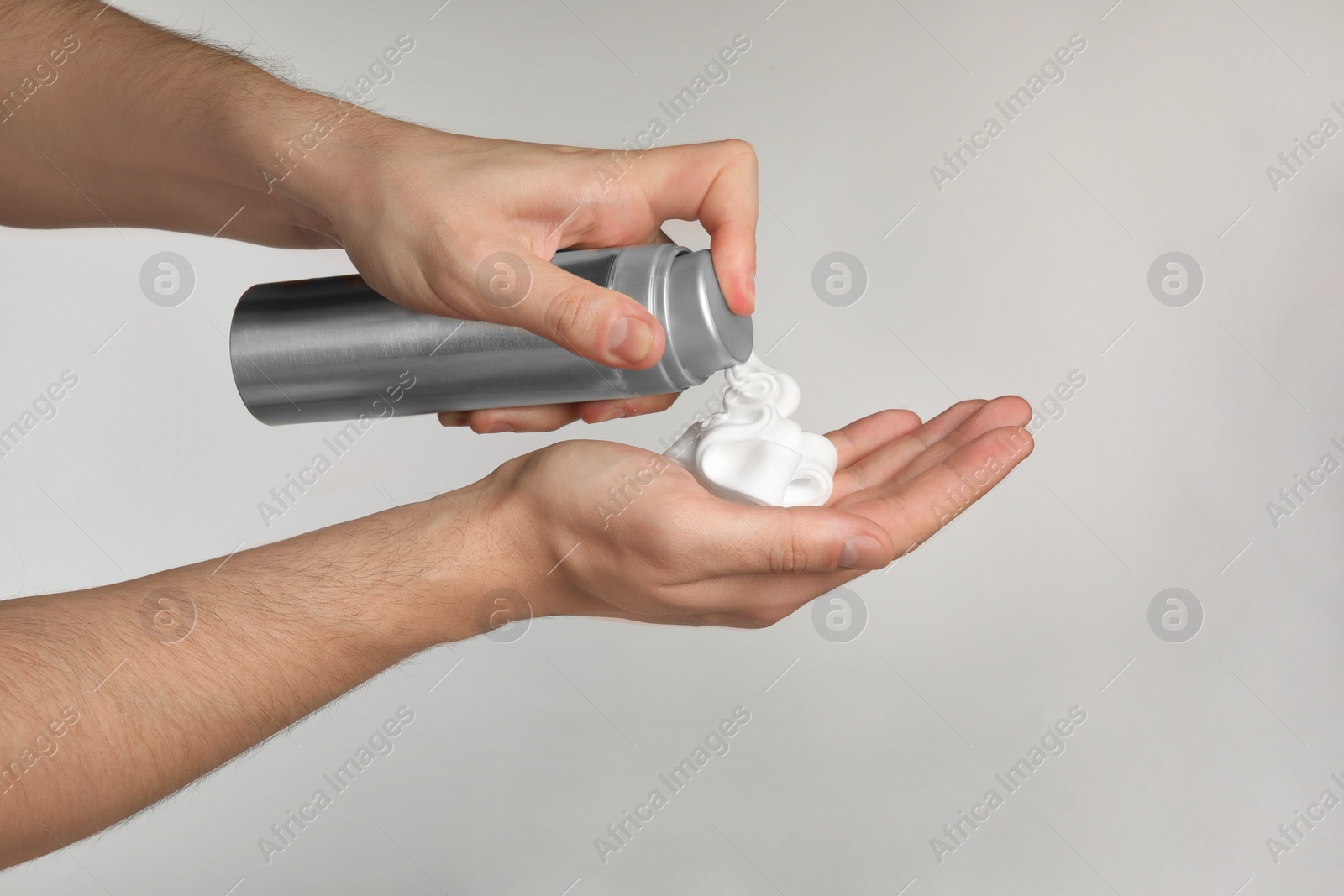 Photo of Man applying shaving foam onto hand on light grey background, closeup