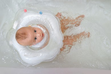 Photo of Cute little baby swimming with inflatable ring in bath, above view