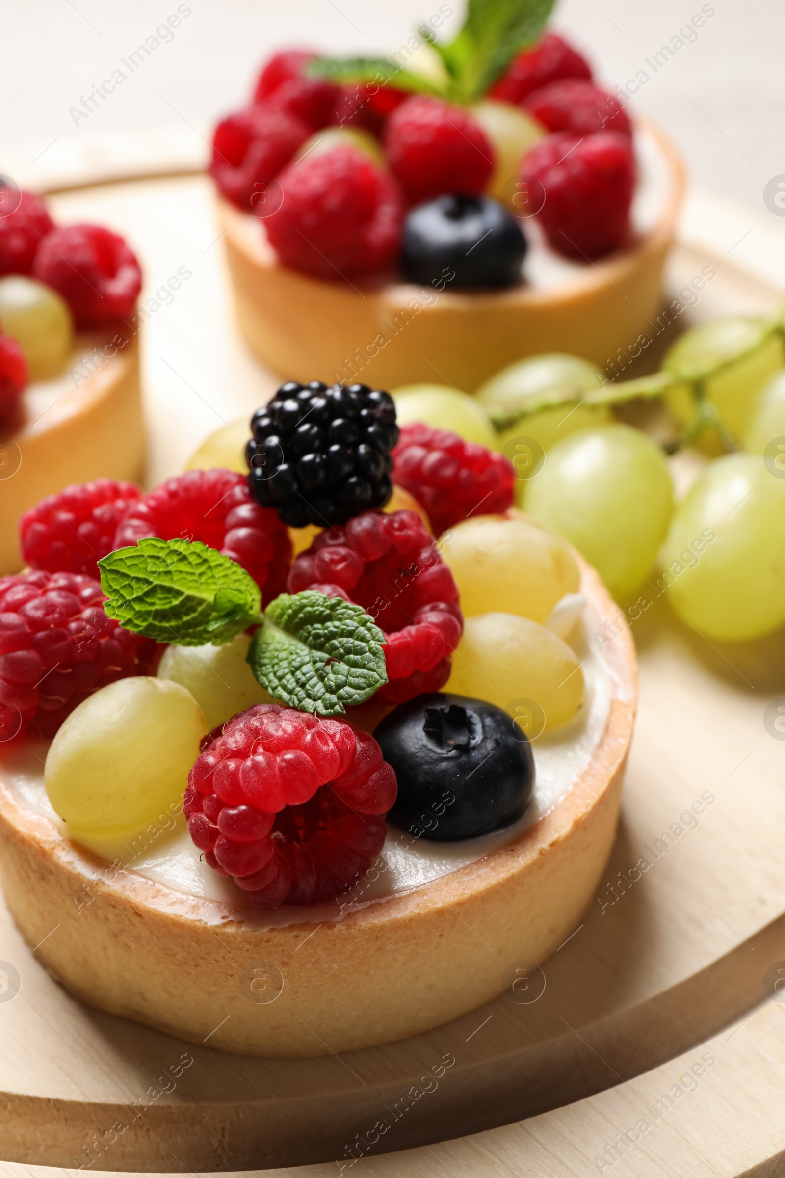 Photo of Delicious tartlets with berries on wooden board, closeup