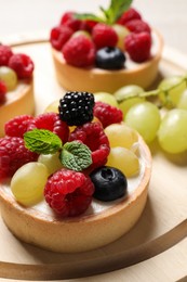Delicious tartlets with berries on wooden board, closeup