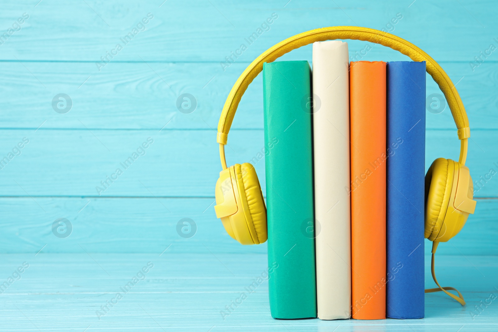 Photo of Books and modern headphones on light blue wooden table. Space for text