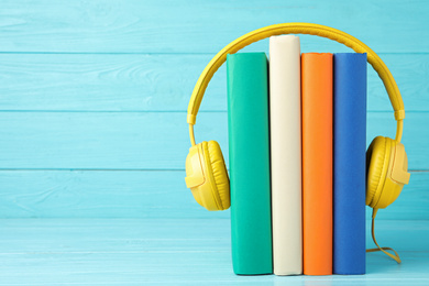 Books and modern headphones on light blue wooden table. Space for text