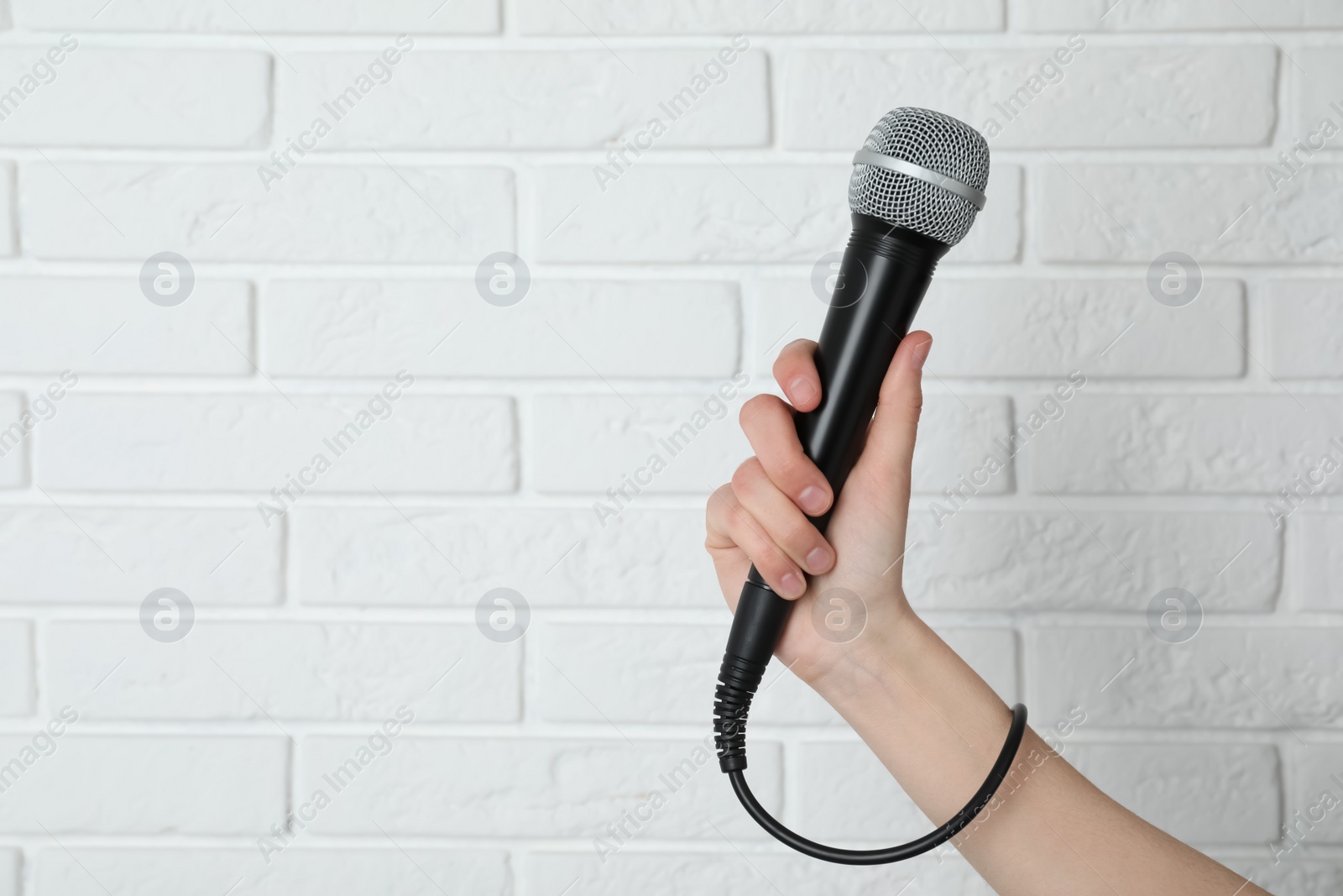 Photo of Woman holding modern microphone near brick wall, closeup. Space for text