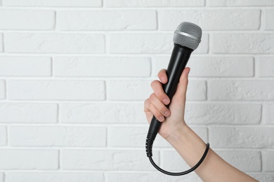 Woman holding modern microphone near brick wall, closeup. Space for text