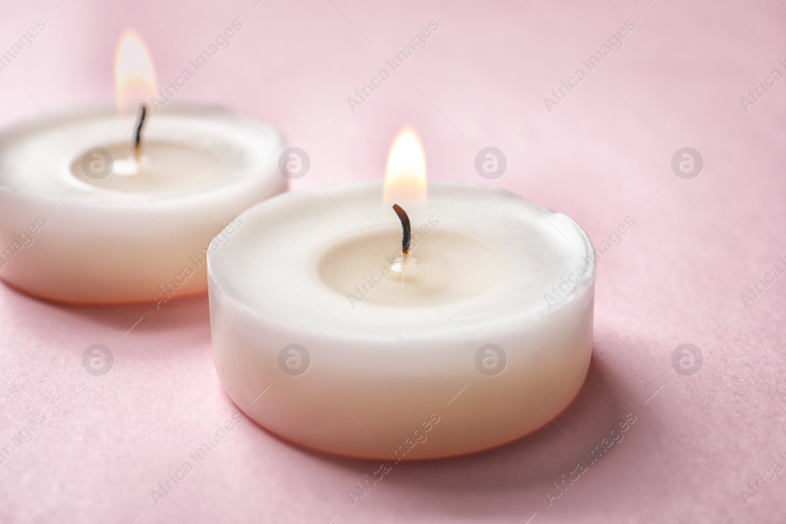 Photo of Small wax candles burning on color background, closeup