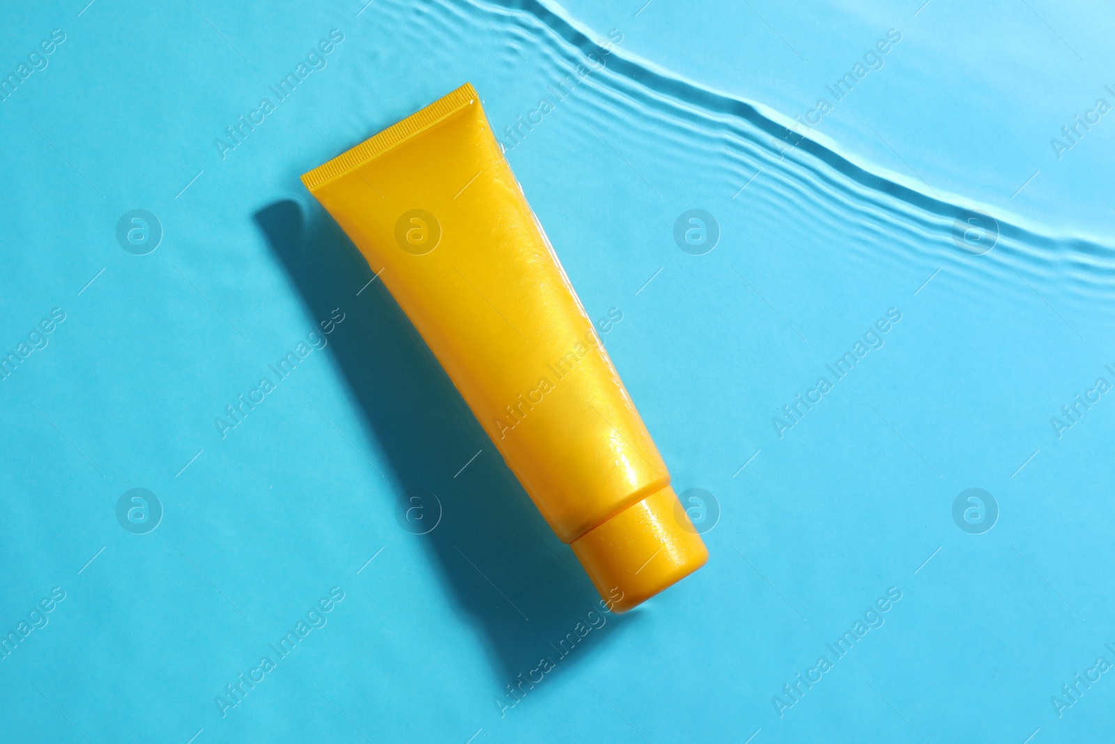 Photo of Tube with moisturizing cream in water on light blue background, top view