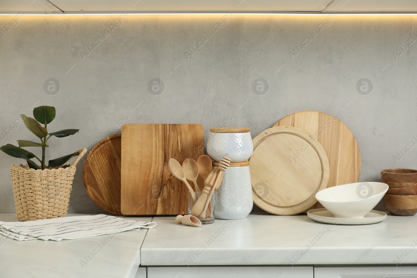 Photo of DIfferent wooden cutting boards, other cooking utensils and houseplant on white countertop in kitchen